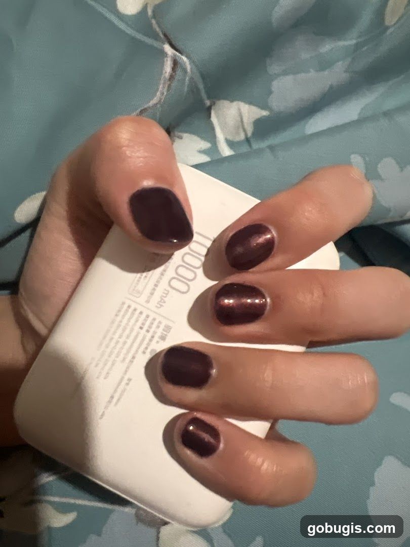 Hand with dark nail polish holding a white power bank
