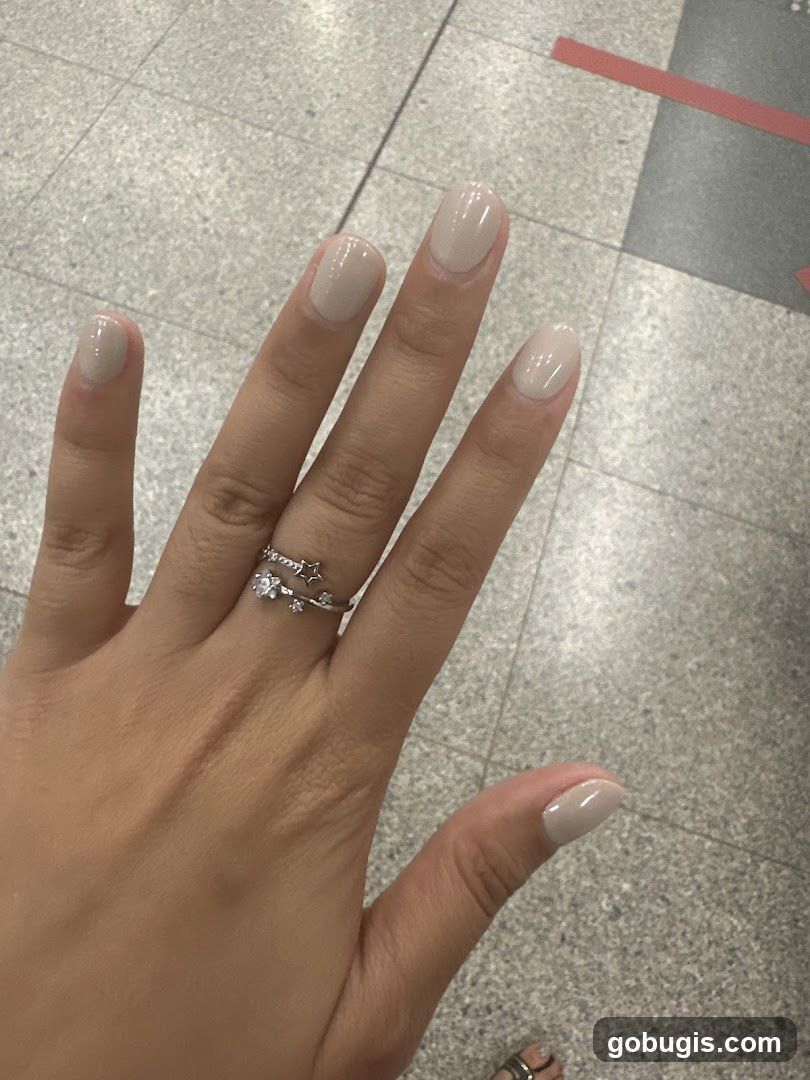 Close-up of a hand with light beige nail polish and a star-themed ring.