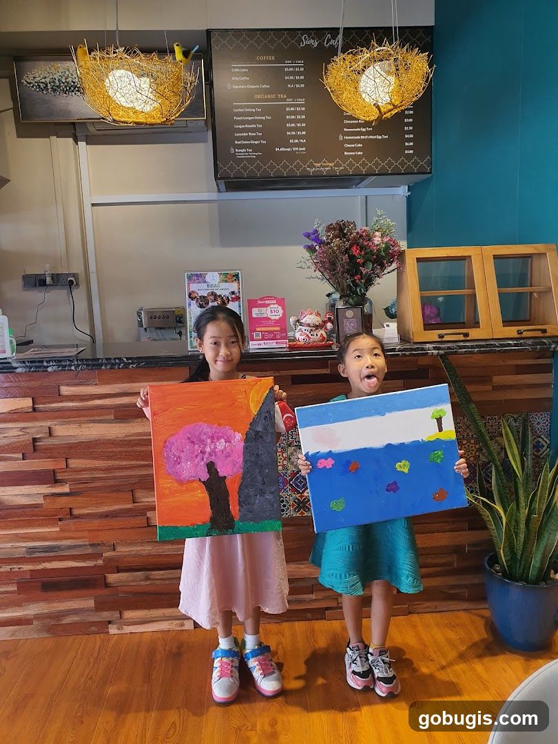 Two girls holding up paintings in a cafe