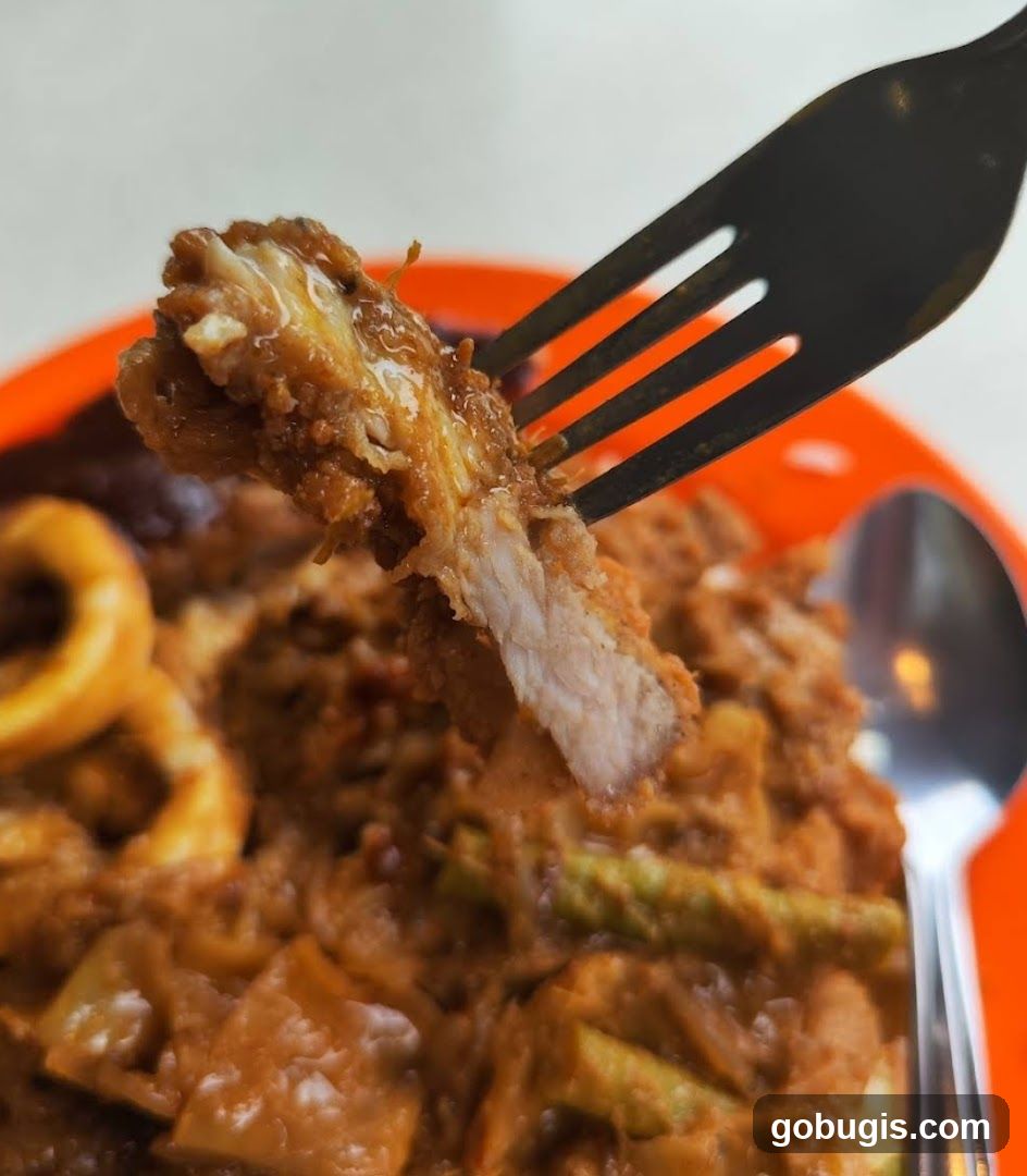 Close-up of a fork lifting a piece of breaded meat from a dish.