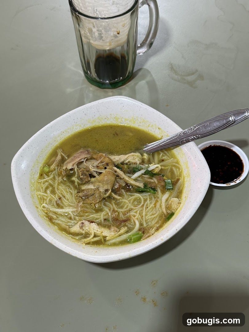 Chicken noodle soup with a side of soy sauce and a drink