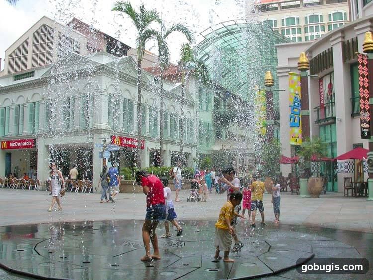 Children playing in a fountain in front of shops