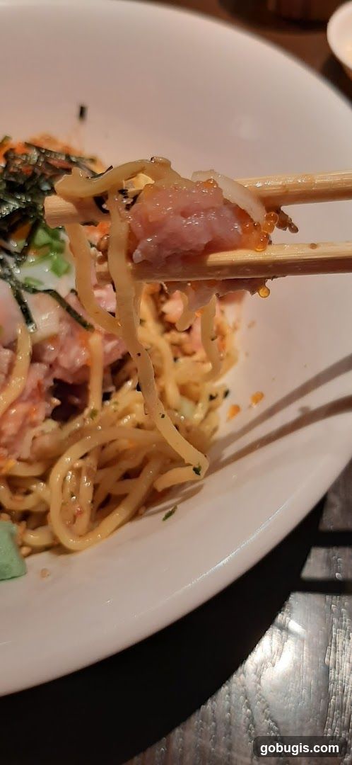 Chopsticks holding a bite of noodles with salmon and roe