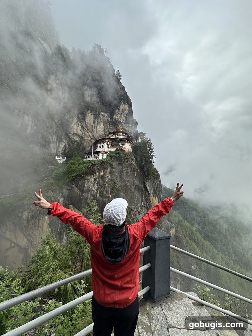 Person with arms outstretched overlooking a monastery on a cliff