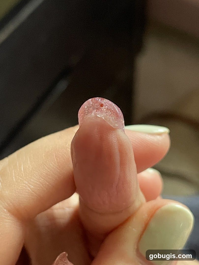 Close-up of a finger with a pink, glittery substance on the tip.