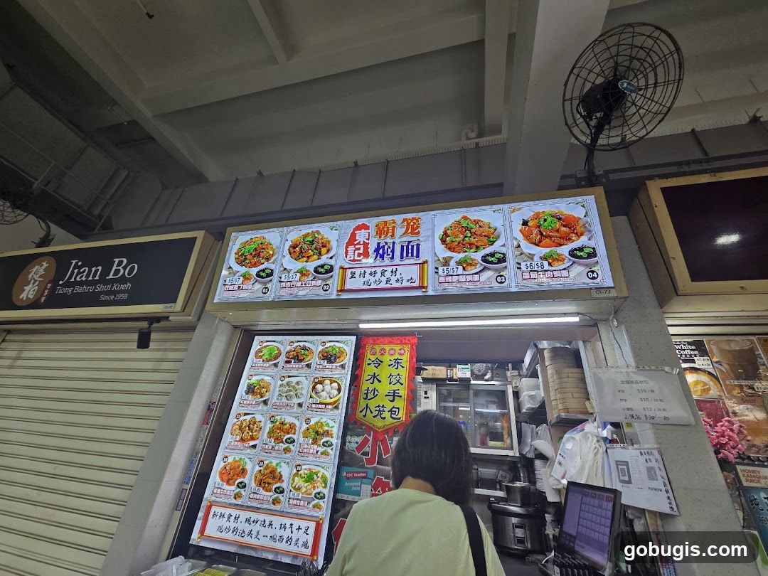 A food stall with illuminated menu boards displaying various dishes. The stall's name,