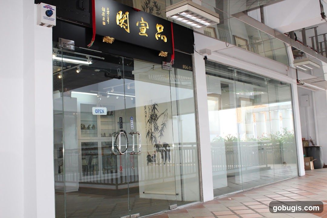 A modern shop front with large glass doors and windows. Above the entrance, a black sign with golden Chinese characters is visible, along with red decorative ribbons. A small white sign indicating "OPEN" hangs on the glass door. Inside, display shelves with items and artwork can be seen. The exterior is clean and well-lit.