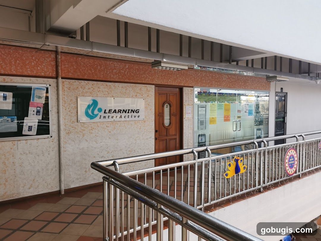 The exterior of a learning center with a sign that reads "LEARNING InterActive" above the entrance. There are glass doors and windows, with various posters and notices displayed inside and on the glass. A wooden door is to the left of the glass entrance.