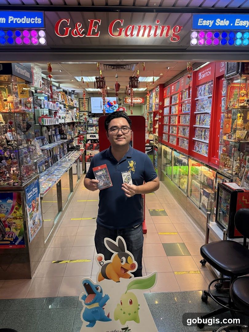 A man stands in the entrance of a video game store, holding two game cases. The store is filled with shelves stocked with video games and accessories. The store's name, "G&E Gaming", is prominently displayed above the entrance. There are also displays of Nintendo Switch games and merchandise. A cardboard cutout of Pokémon characters is in the foreground.