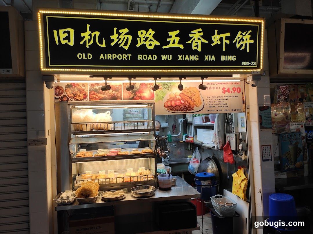 A food stall with a prominent sign displaying the business name in Chinese and English. The stall features a display of various fried food items and a menu board with a recommended set meal.