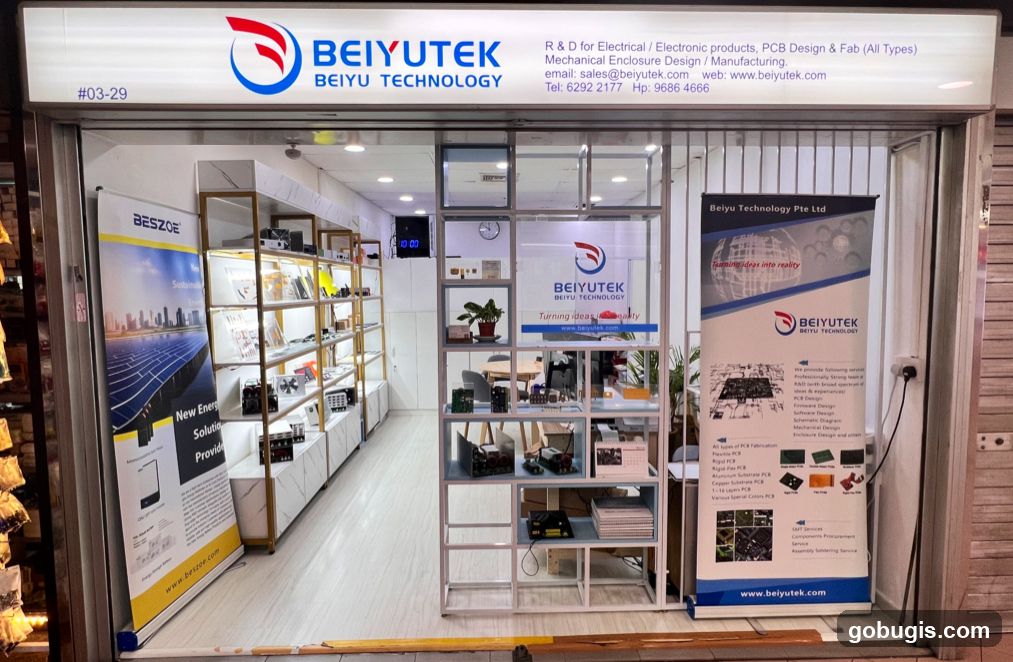 The storefront of Beiyutek Beiyu Technology, a company specializing in R&D for electrical and electronic products, PCB design, and manufacturing. The facade features a prominent illuminated sign with the company logo and name, along with contact information. Inside, shelves display electronic components and products. Banners with company information and services are also visible.