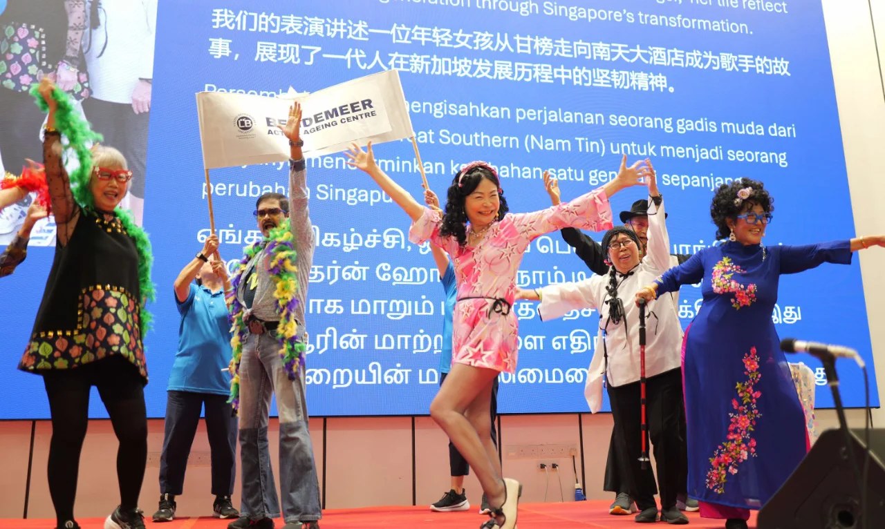 Seniors on stage at the National Museum, one holding a Bendemeer Active Ageing Centre flag, during the From Kampong to Catwalk talent show