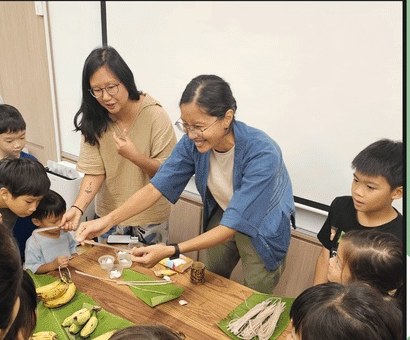 Wild Dot facilitators and children around a wooden table with bananas, banana leaves and small jars during a plant-colour workshop