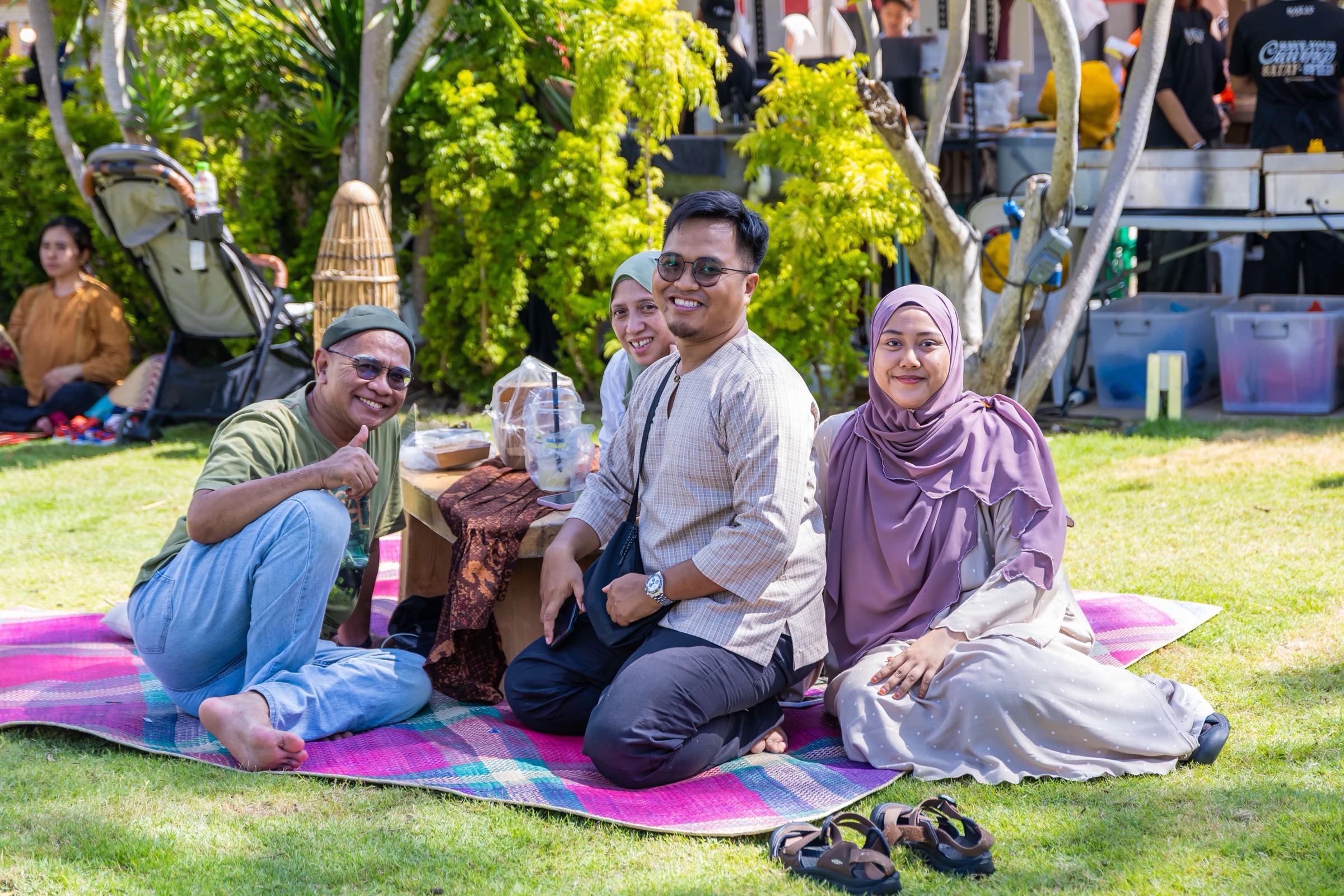 Families sitting on a tikar on the Malay Heritage Centre lawn with food stalls behind the trees