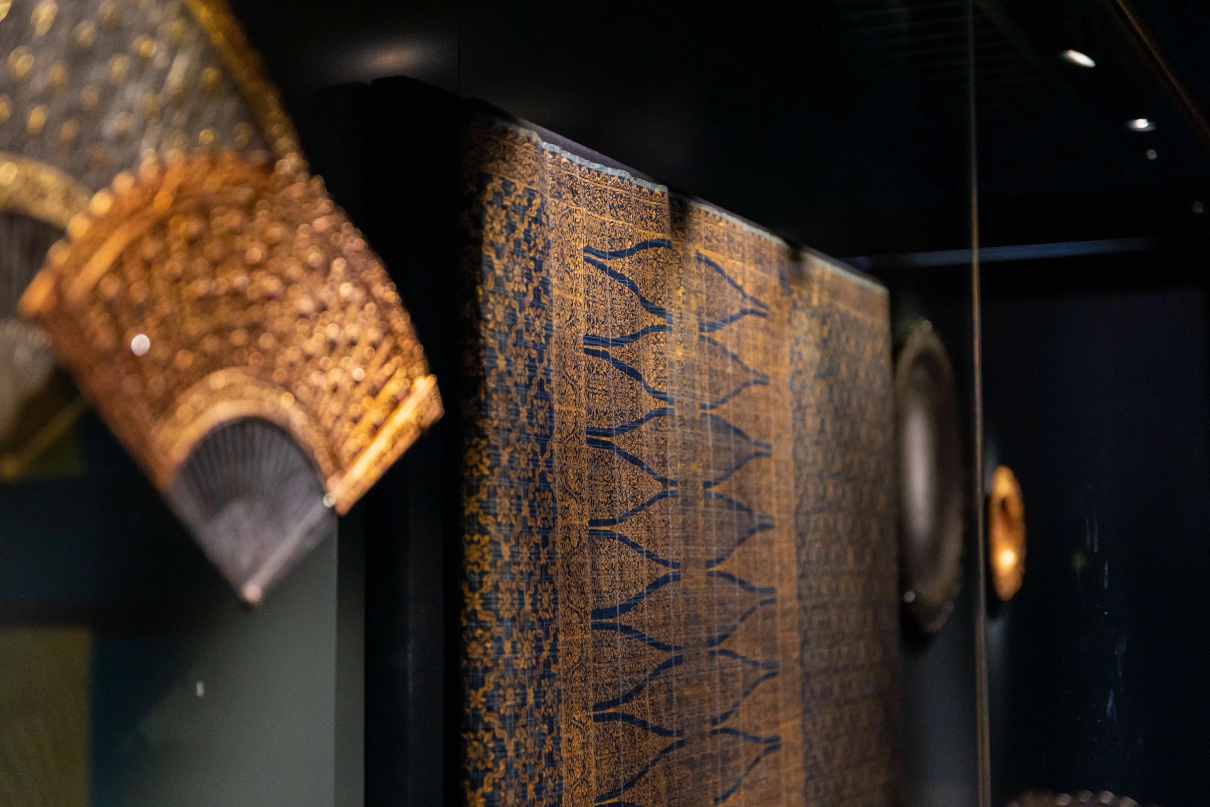 Gold songket textile and ornate fans in a glass case at the Malay Heritage Centre galleries